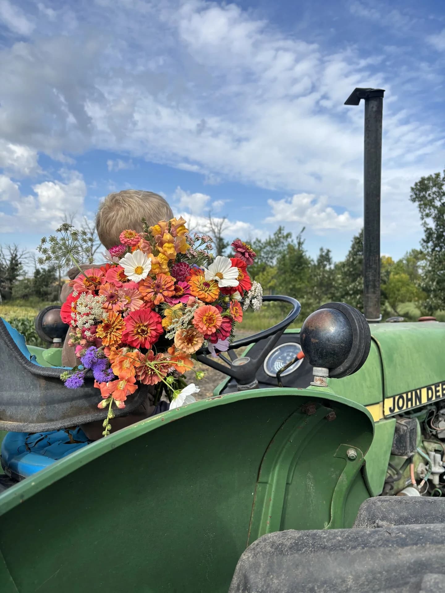 A vintage tractor at the edge of the garden with a bucket of fresh-cut flowers beside it.