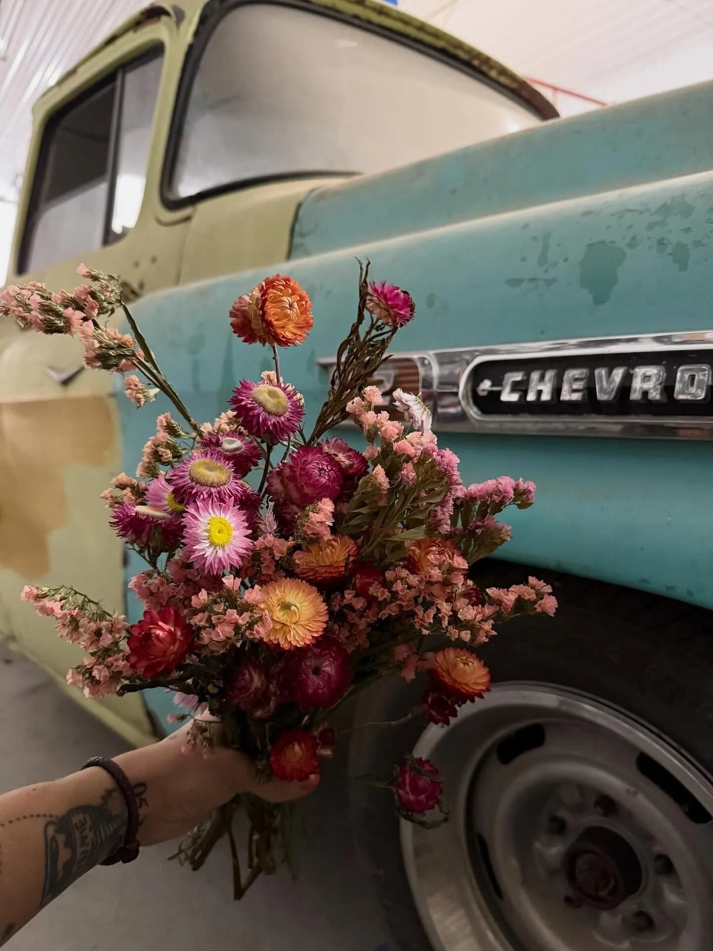 The Flower Truck — a teal vintage Chevy pickup — with a hand-tied bouquet of strawflowers held in front of it.