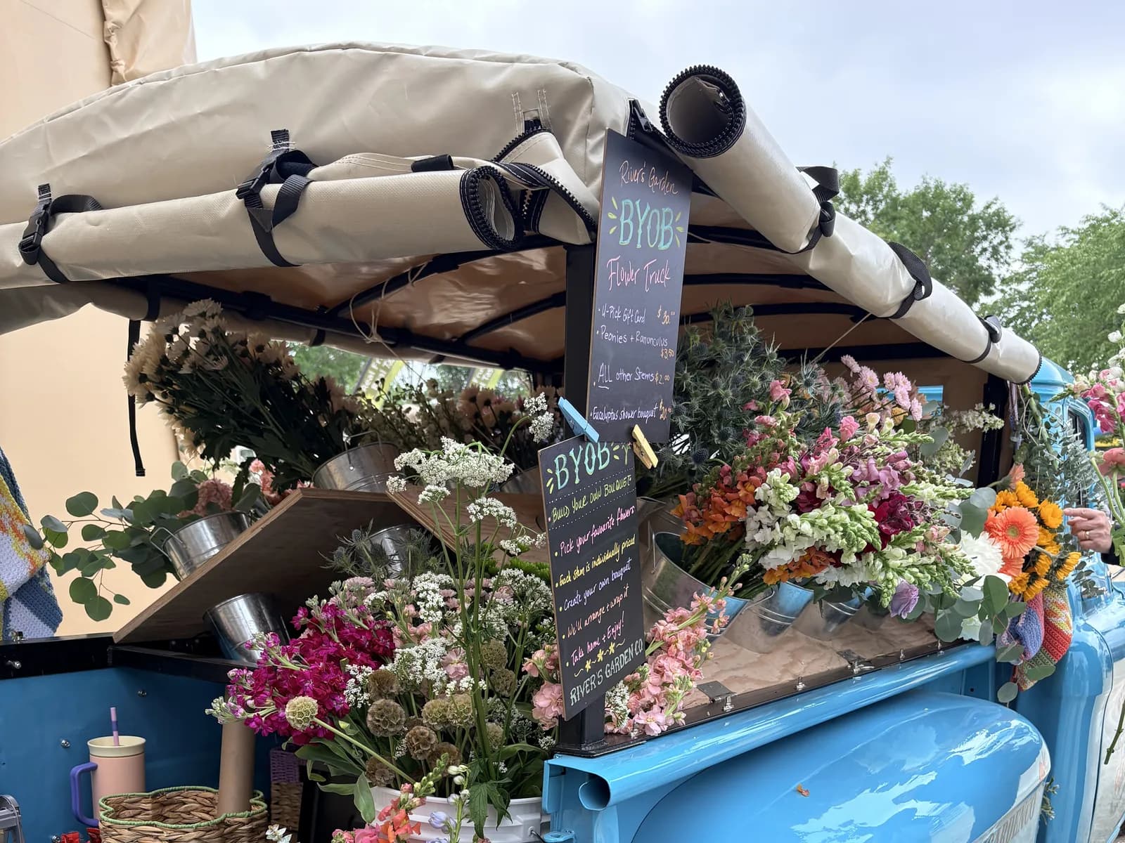 Truck bed loaded with buckets of bouquets — orange ranunculus, pink peonies, snapdragons — against the freshly-painted teal fender.